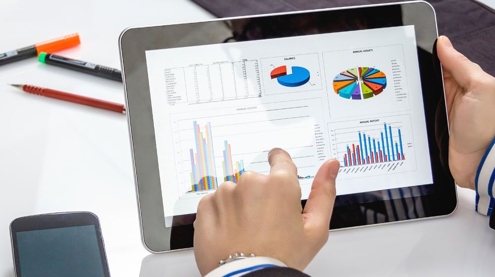 Hand pointing to tablet with exam data in coloured charts